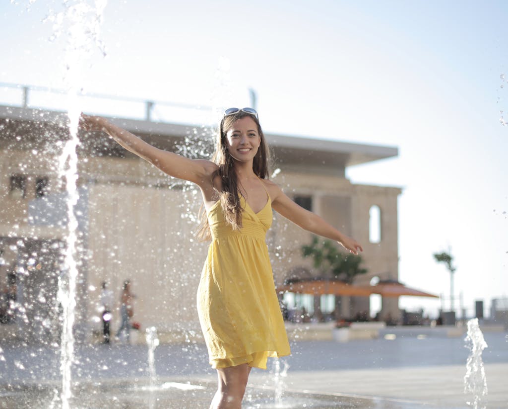 Woman in Yellow Dress Standing on Water Fountain